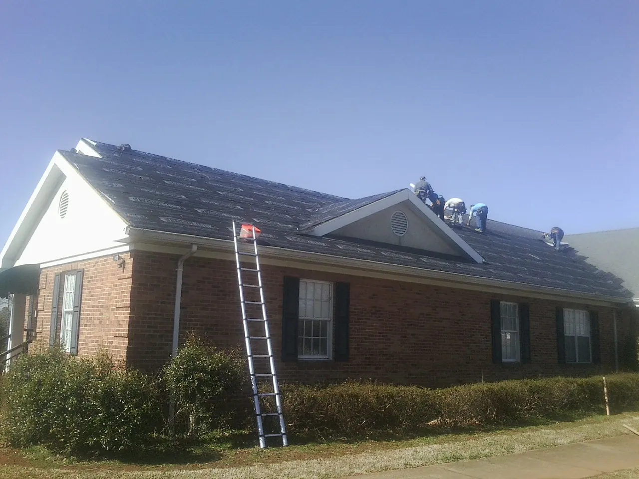 Crew tearing shingles off a brick ranch roof with a ladder set — Emergency Roof Repair work by our crew in Glendale Heights