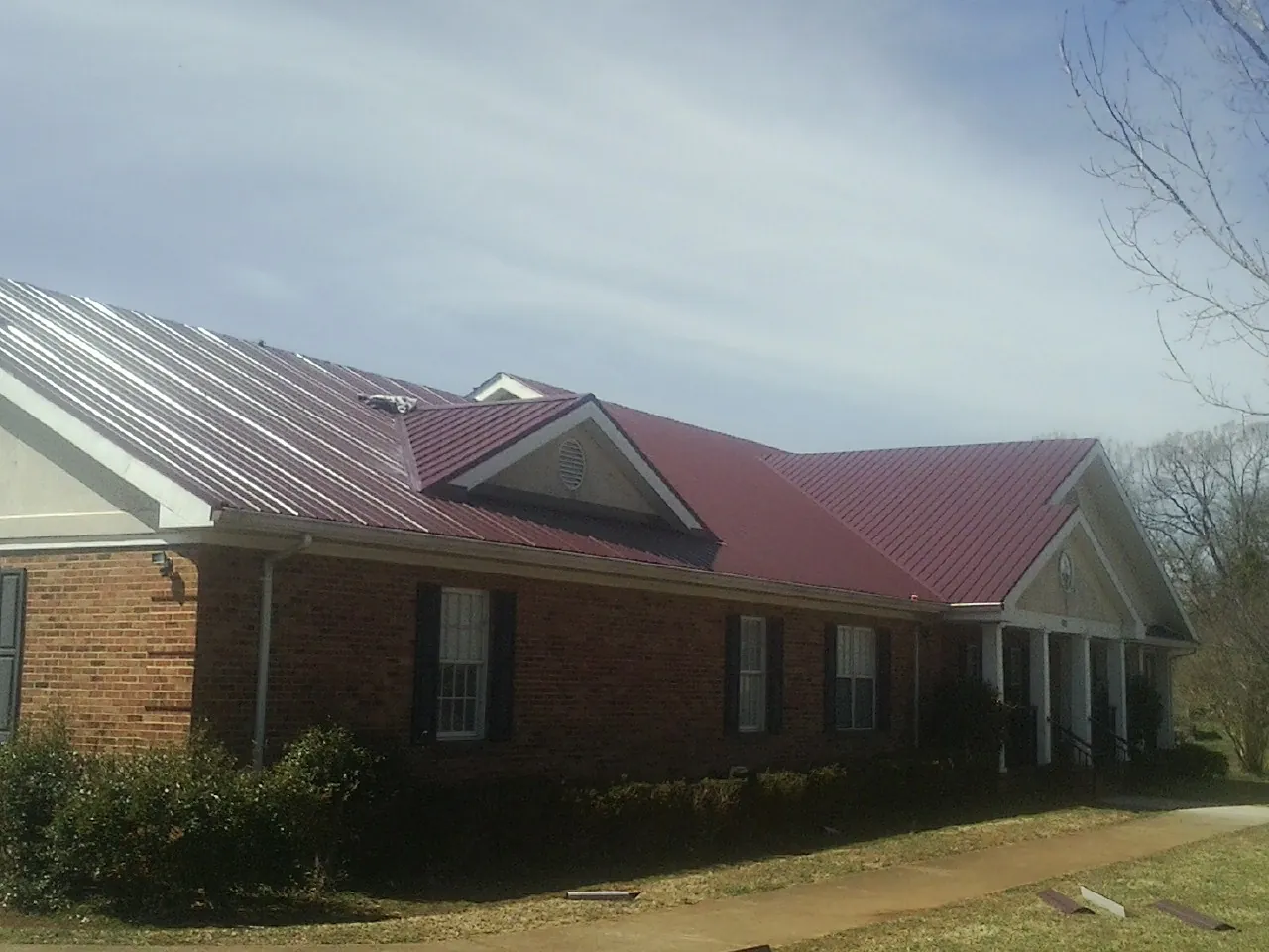 Red metal roof with gabled entries on a long brick building, from a Hail Damage Roof Repair job in Glendale Heights