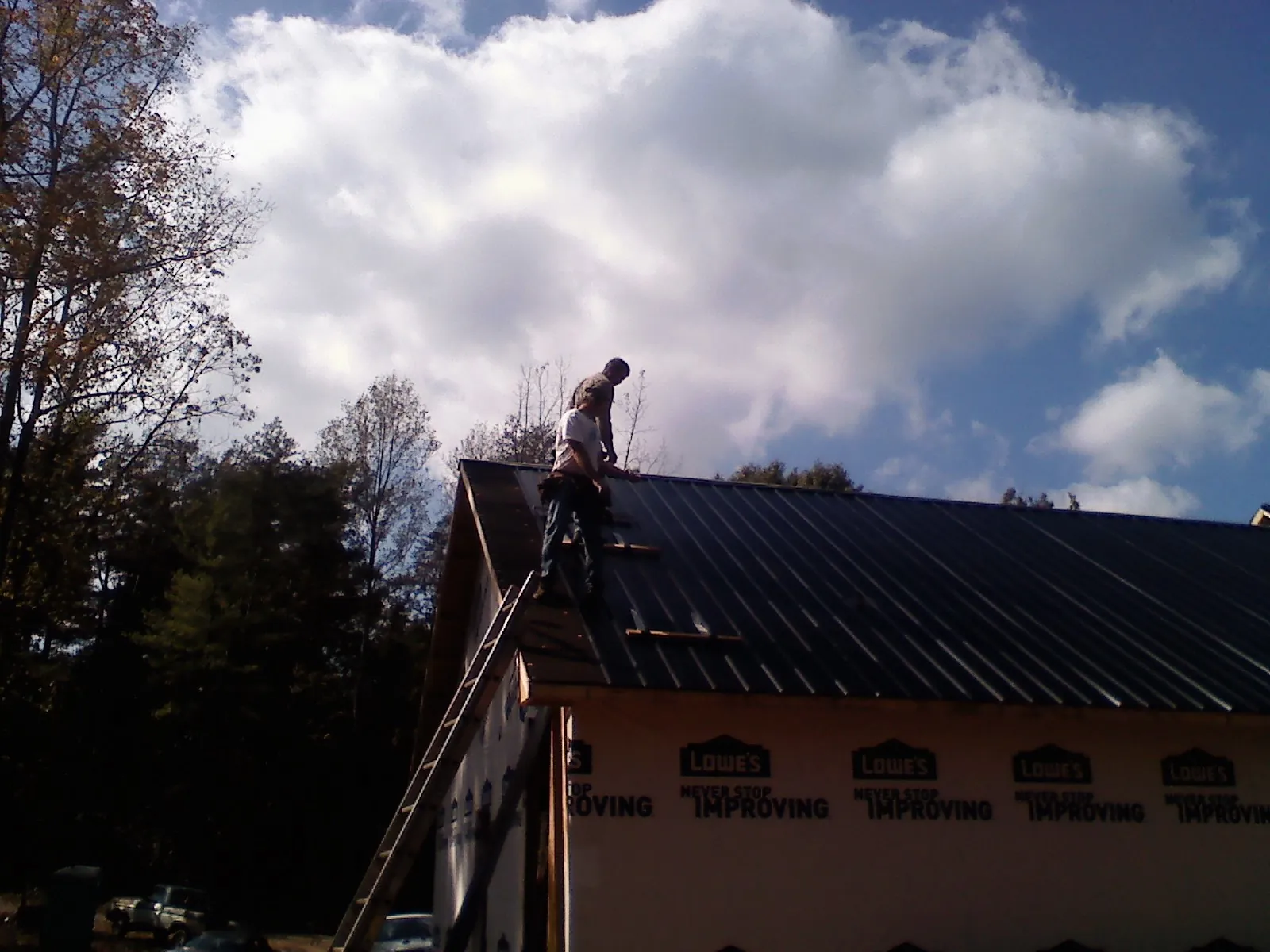 Roofer fastening dark metal panels high against a cloudy sky, from a Roof Inspection job in Glendale Heights