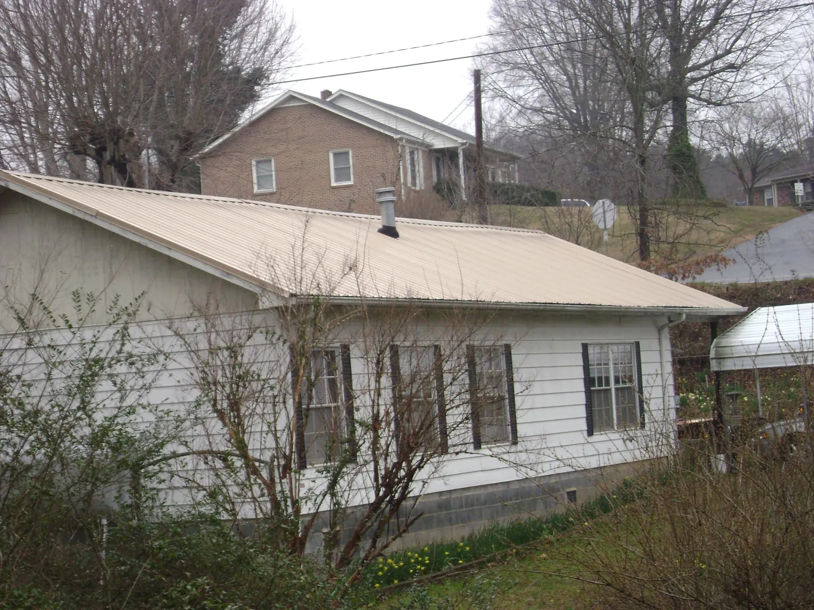 Tan metal roof on a white sided house set into a hillside — Commercial Roofing by Roofing Brothers in Glendale Heights